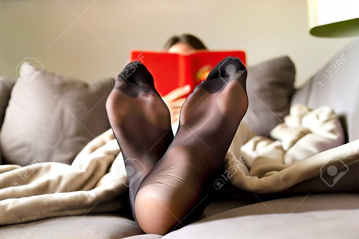 A portrait of a woman's feet wearing black nylon pantyhose or stockings with reinforces toes on a cozy couch in a living room trying to relax after a hard day of work.