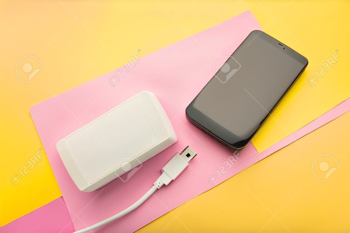 Portable power bank with usb cable on pink and yellow background. top view