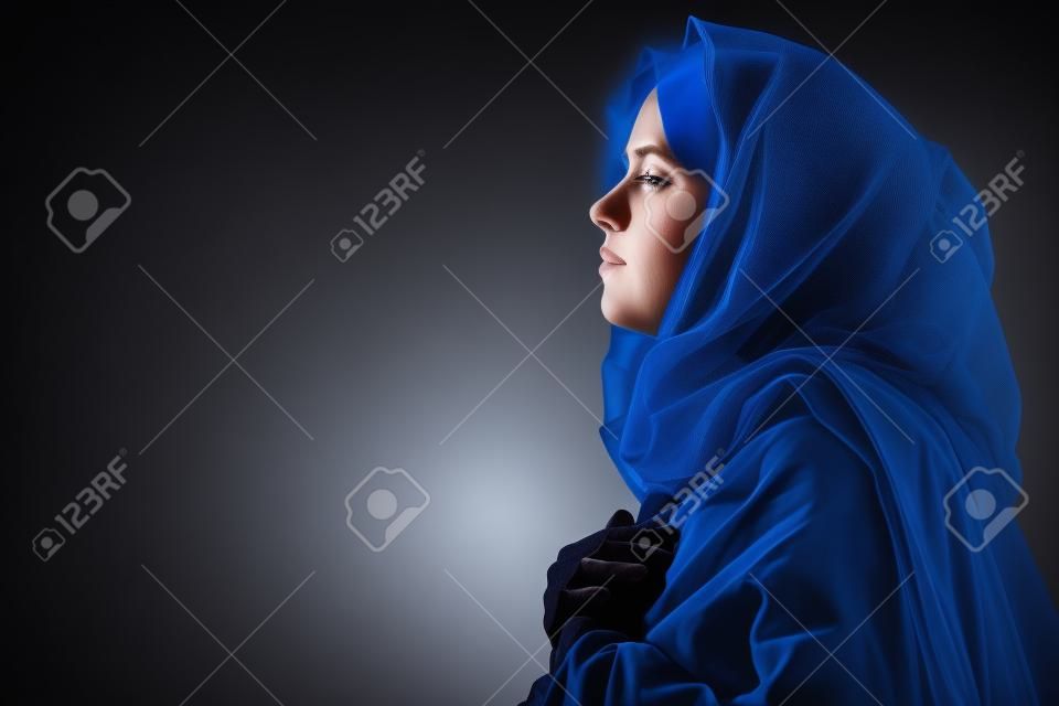 聖母マリアは黒い背景に青いベールに祈っ