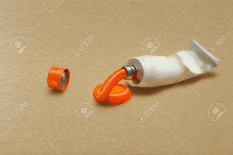 Um tubo espremido de tinta a óleo laranja na frente do fundo branco. Ao lado do tubo está a tampa.