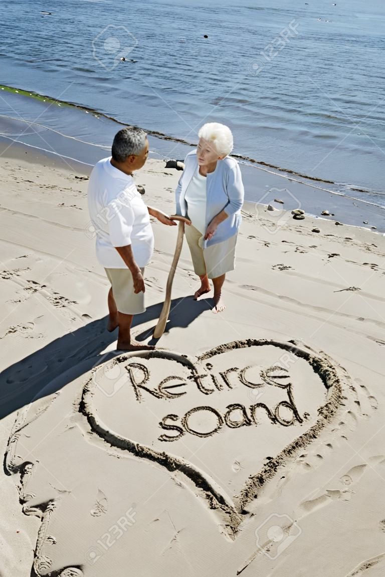 快樂的退休夫婦在海灘上寫有棍子在沙地上。