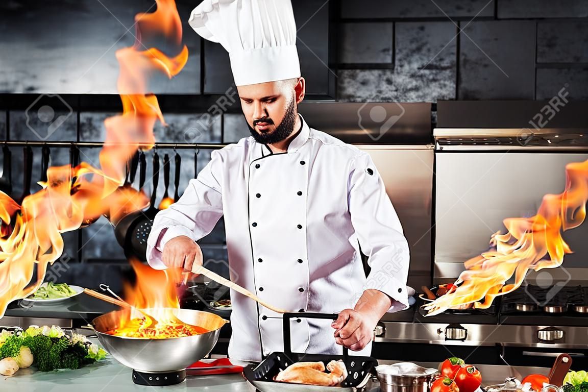 Chef cook food with fire at kitchen restaurant. Cook with wok at kitchen. Chef male in uniform hold wok with fire.