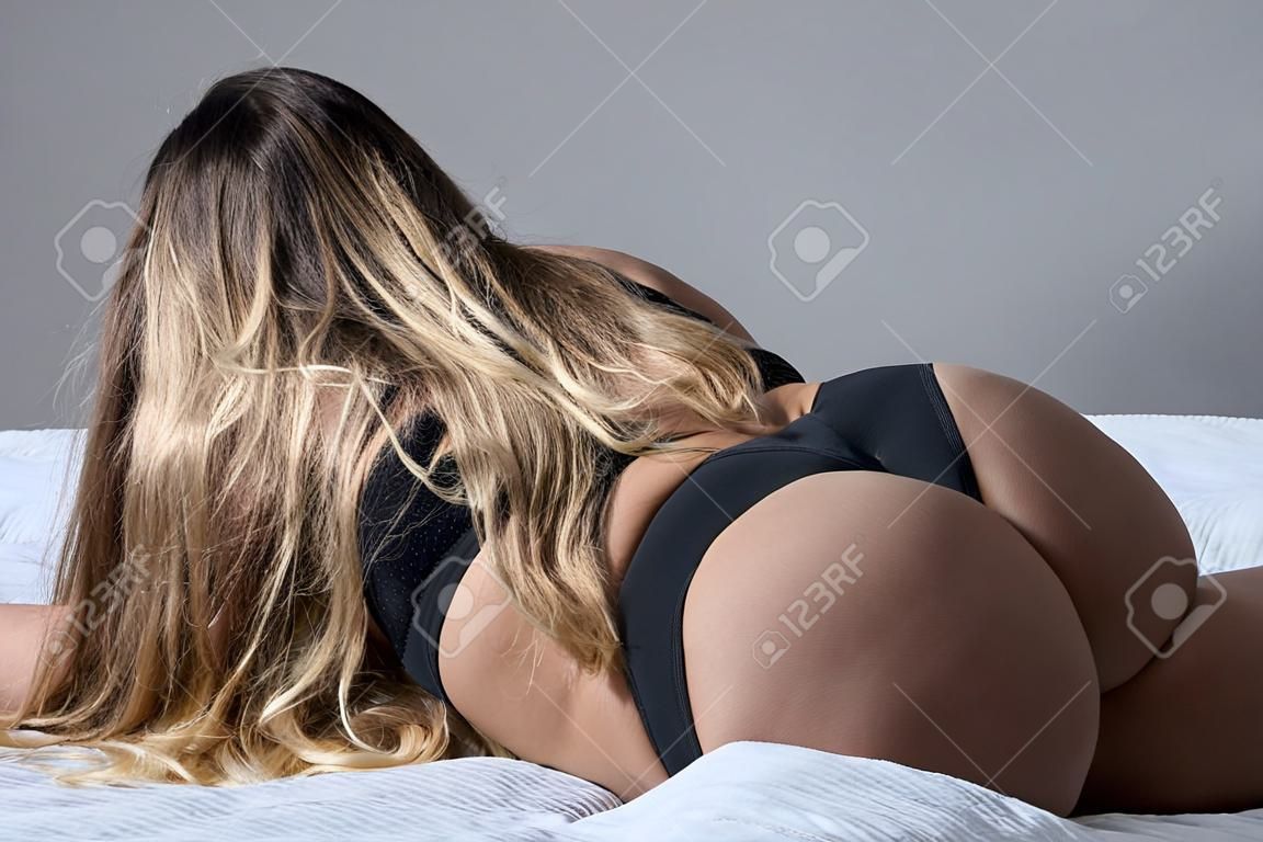 A blonde with long hair in black underwear is lying on the bed. Rear view of a girl in thong sleeping on a gray plaid. A figured woman with wide hips, a big booty and a narrow waist. Close-up.