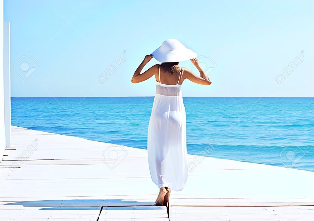 Woman in white dress on a wooden pier on summer.  Sea and sky background. Vacation, traveling and freedom concept.