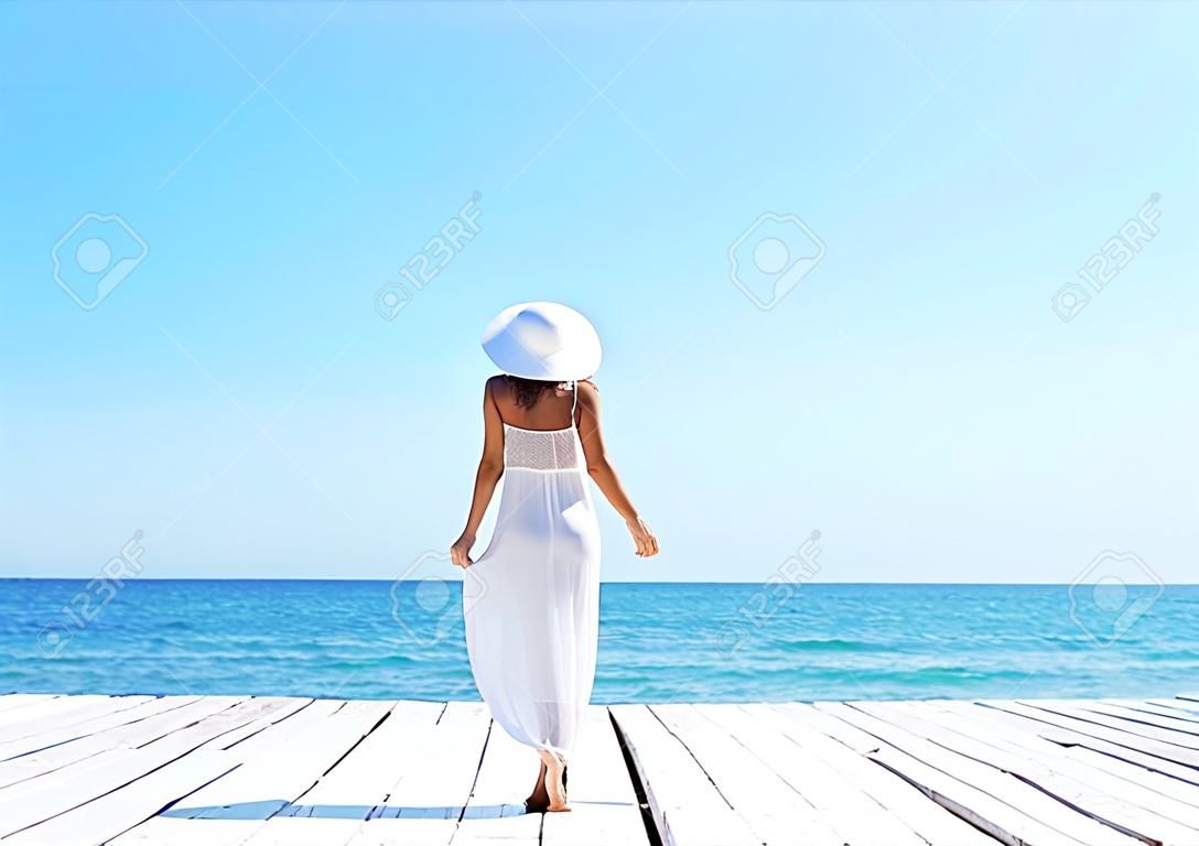 Woman in white dress on a wooden pier on summer.  Sea and sky background. Vacation, traveling and freedom concept.