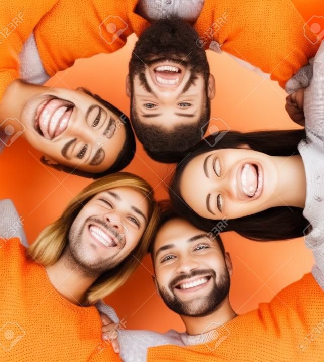 Happy, smiling friends standing together and looking at camera over orange background.