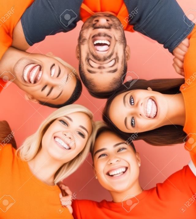 Amici felici e sorridenti in piedi insieme e guardando la fotocamera su sfondo arancione.