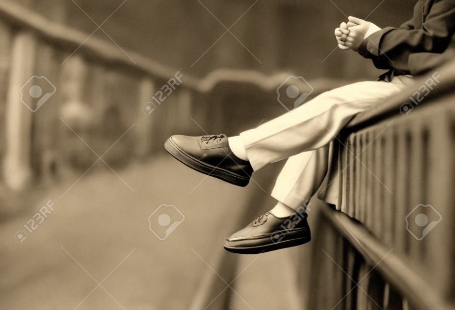un ragazzo seduto da solo con i piedi rivolti verso il basso in tono vintage