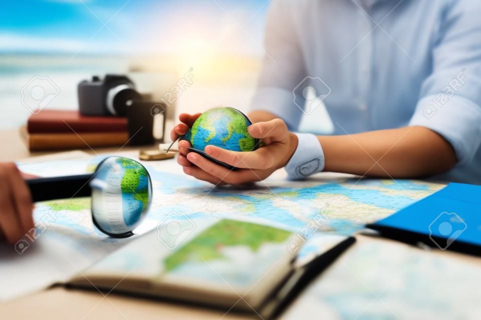 Globus, ganze Welt in Händen und Kompass, Lupe und Buch auf der Streckenkarte auf dem Tisch. Reise-, Abenteuer- und Entdeckungskonzept.