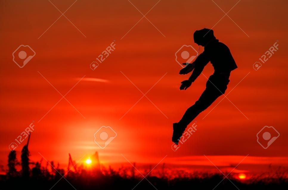 Chico saltando por encima de puesta de sol.