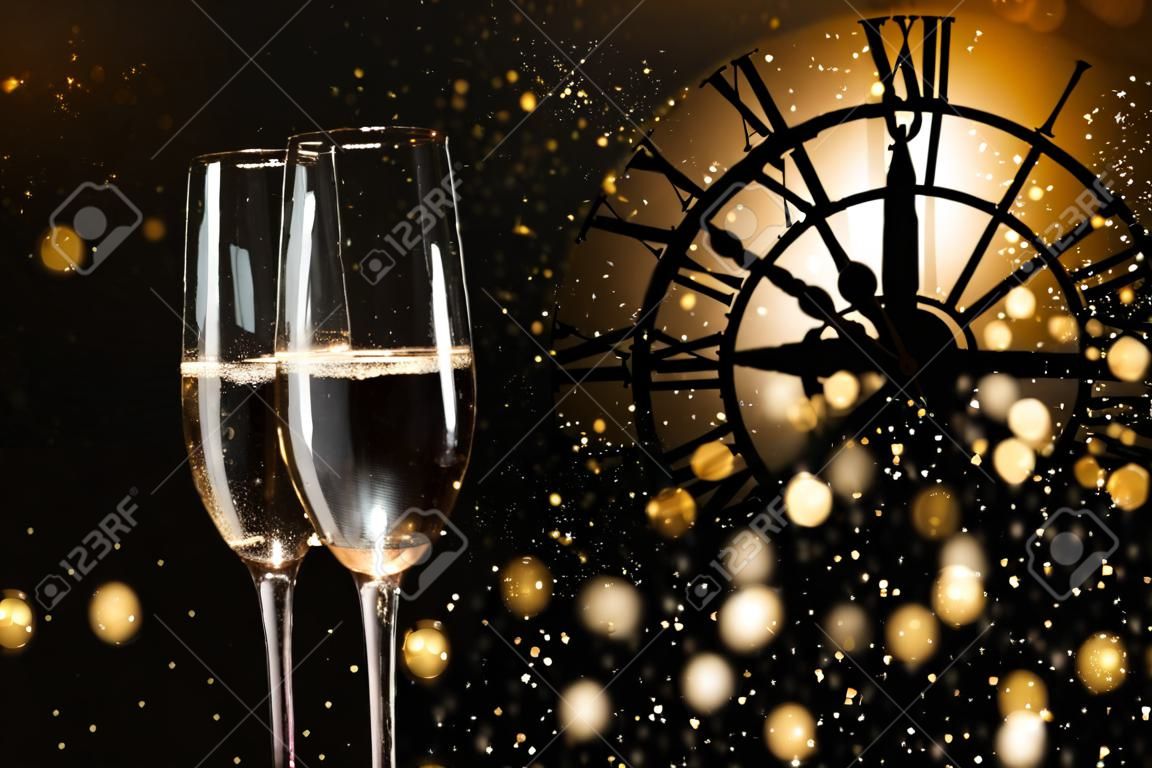 New year congratulations with champagne and a clock in dark background with snowflakes and golden bokeh