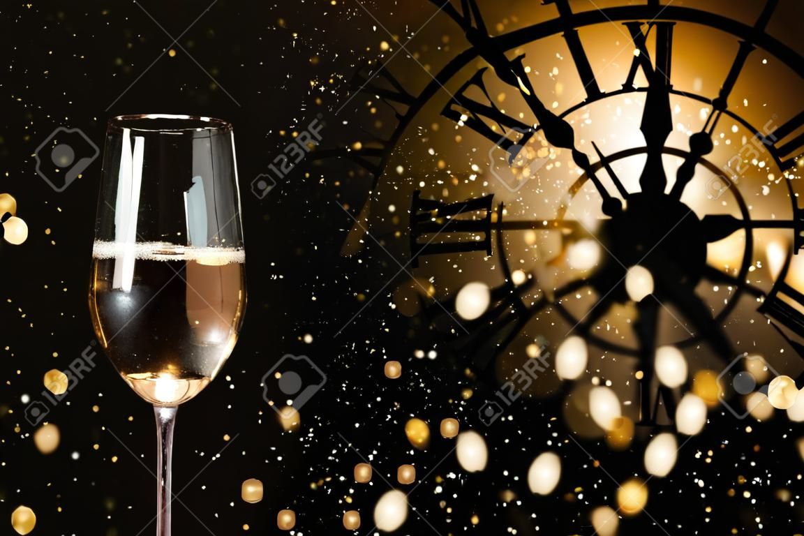New year congratulations with champagne and a clock in dark background with snowflakes and golden bokeh