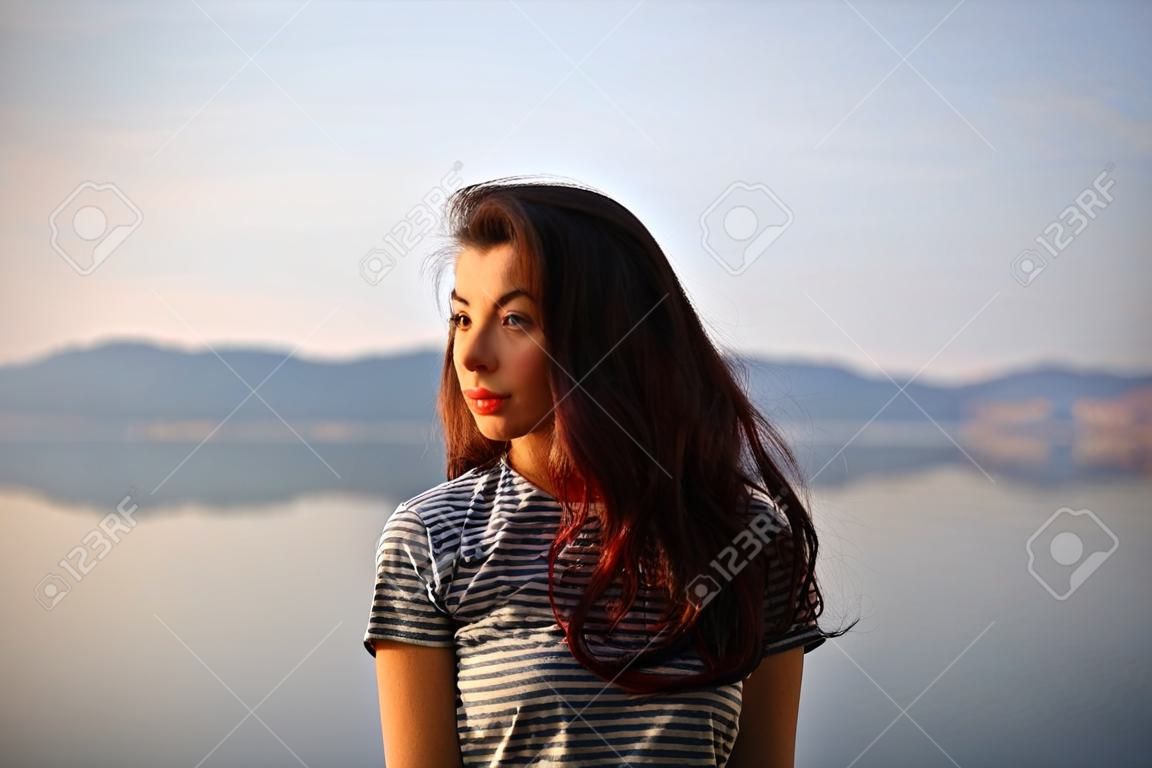 Girl on the background of the lake. Sunset or sunrise.