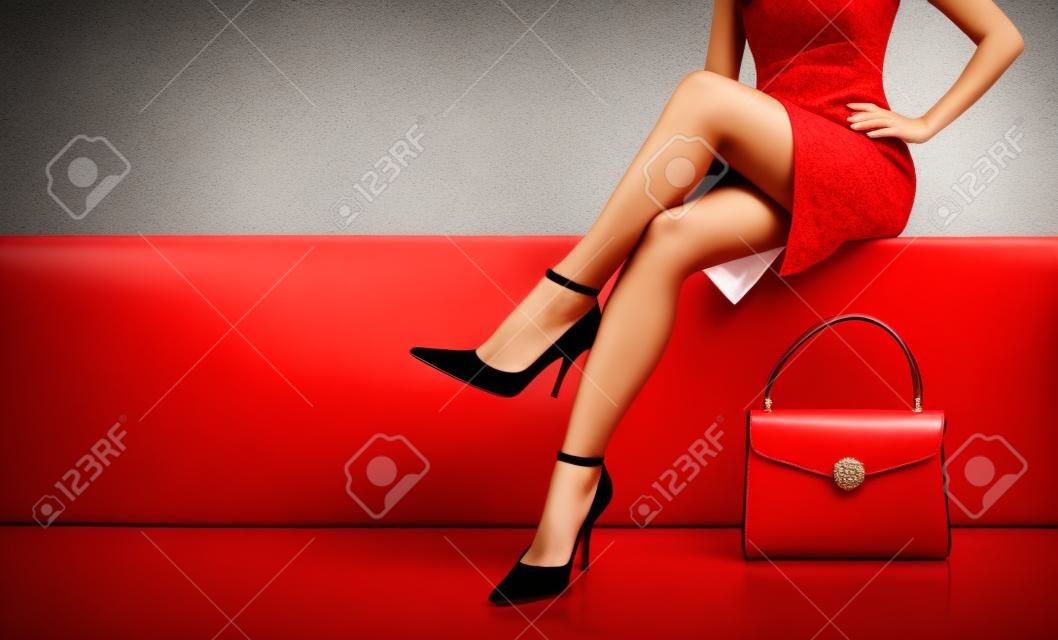Szép lábak, nő, fárasztó, piros ruha, fekete pénztárca kézi táska, magas sarkú cipő ül a fehér padon. copyspace.