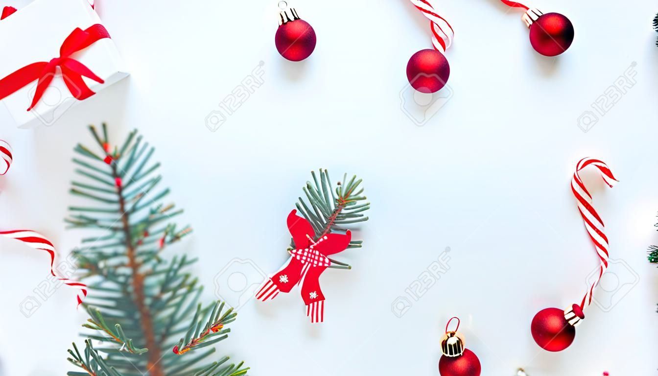Weihnachtskomposition. Weiße Geschenkbox mit rotem Band, Neujahrskugeln, Süßigkeiten und Winterbaum in Weihnachtskomposition auf weißem Hintergrund für Grußkarten. Flache Lage, Draufsicht, Kopierbereich