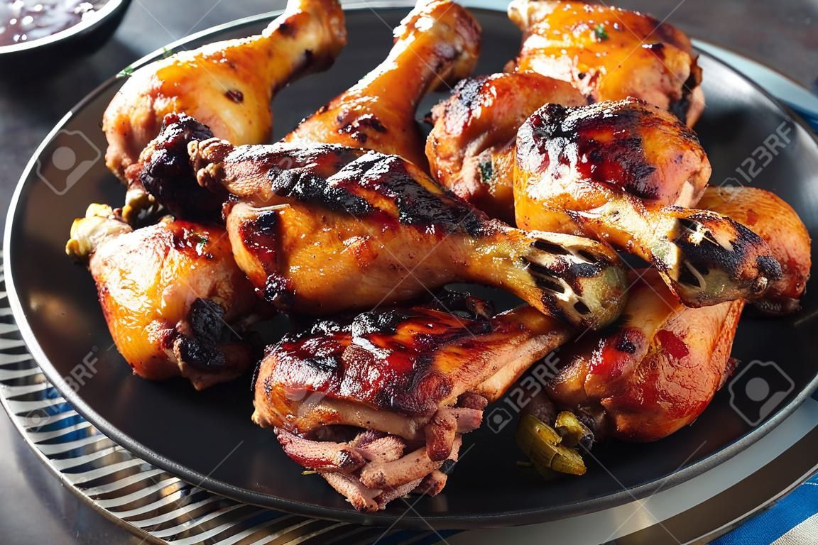 hot Grilled Jamaican Jerk Chicken drumsticks and thighs on a black plate on a concrete table, horizontal view from above, close-up