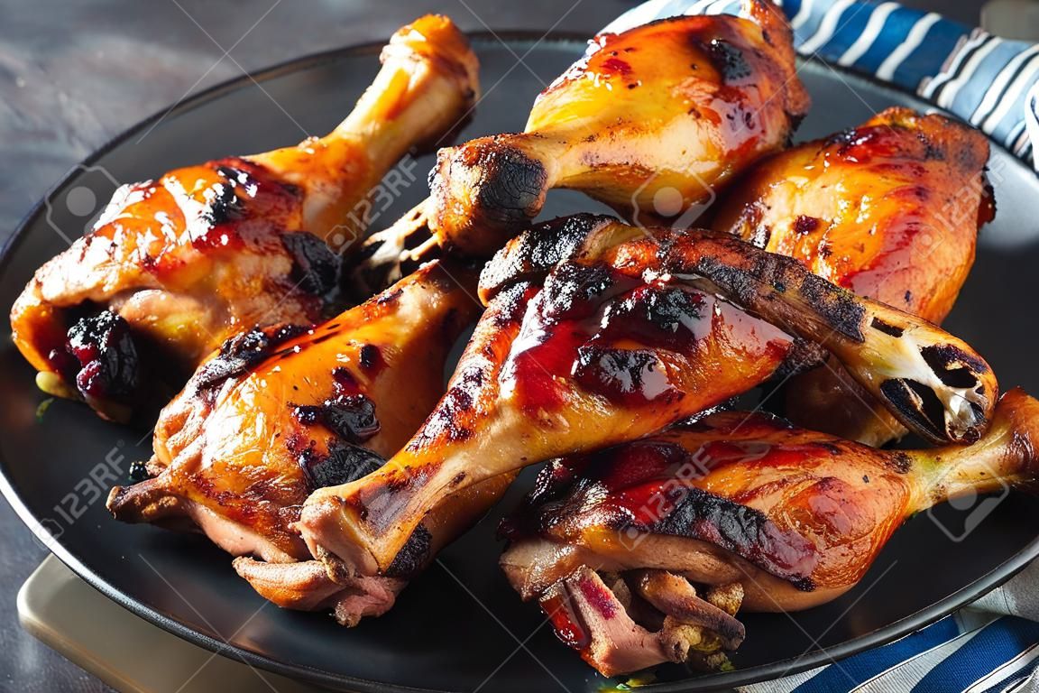 Pilons et cuisses de poulet jamaïcain Jerk grillé chaud sur une plaque noire sur une table en béton, vue horizontale d'en haut, gros plan