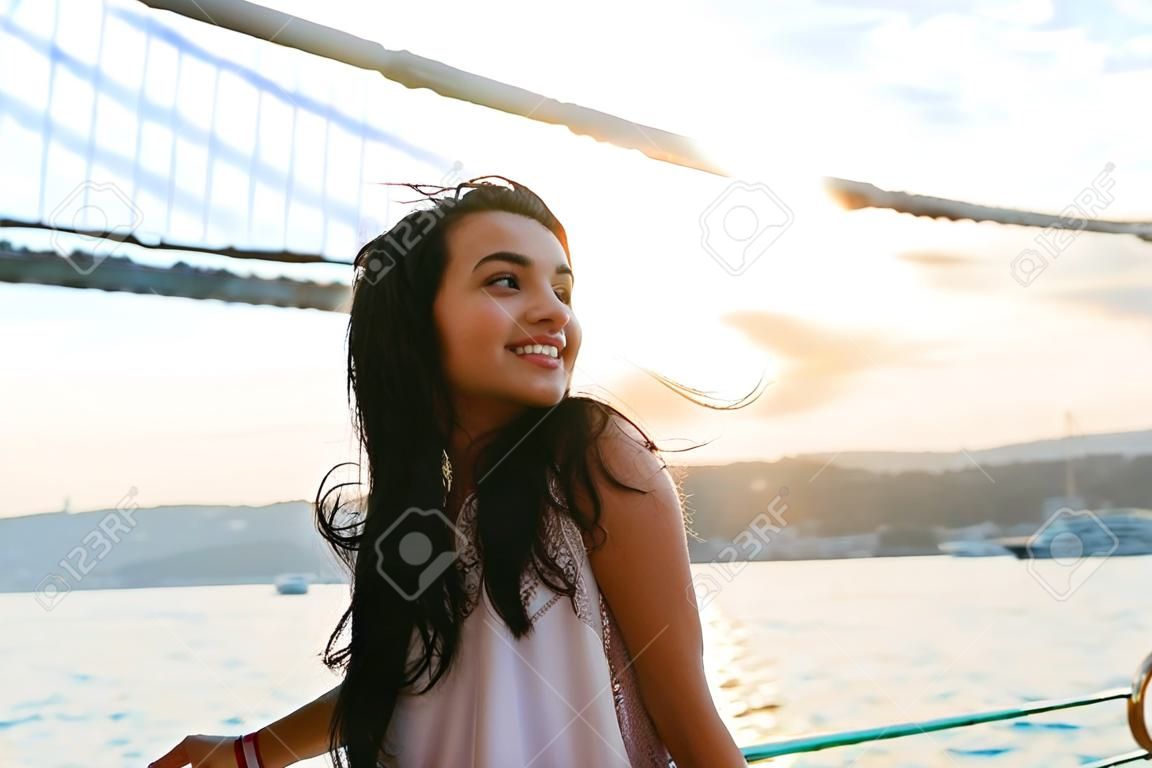 Young girl traveler relaxes while cruising on a yacht, looking at sunset and ocean, bridge on background. Bridge over the Bosphorus in the city of Istanbul