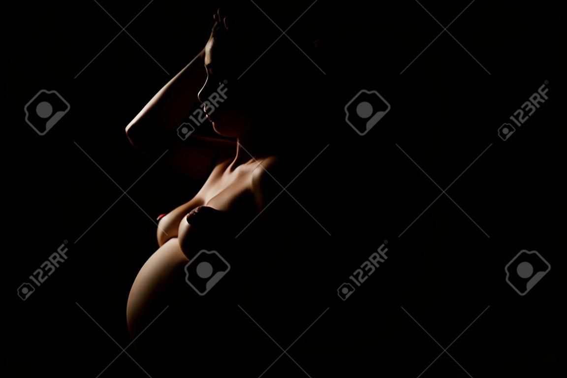 Glückliche schwangere Frau auf dunklem Hintergrund, isolierte Silhouette