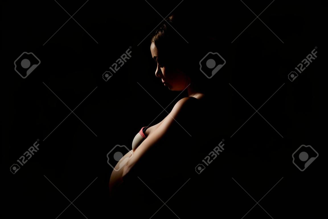 Mujer embarazada feliz sobre fondo oscuro, silueta aislada