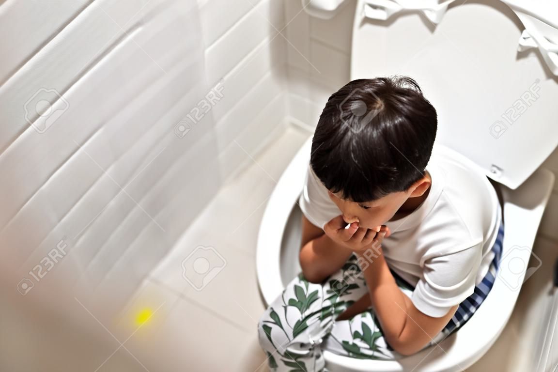 Chłopiec siedzi w toalecie i cierpi na zaparcia lub hemoroidy.