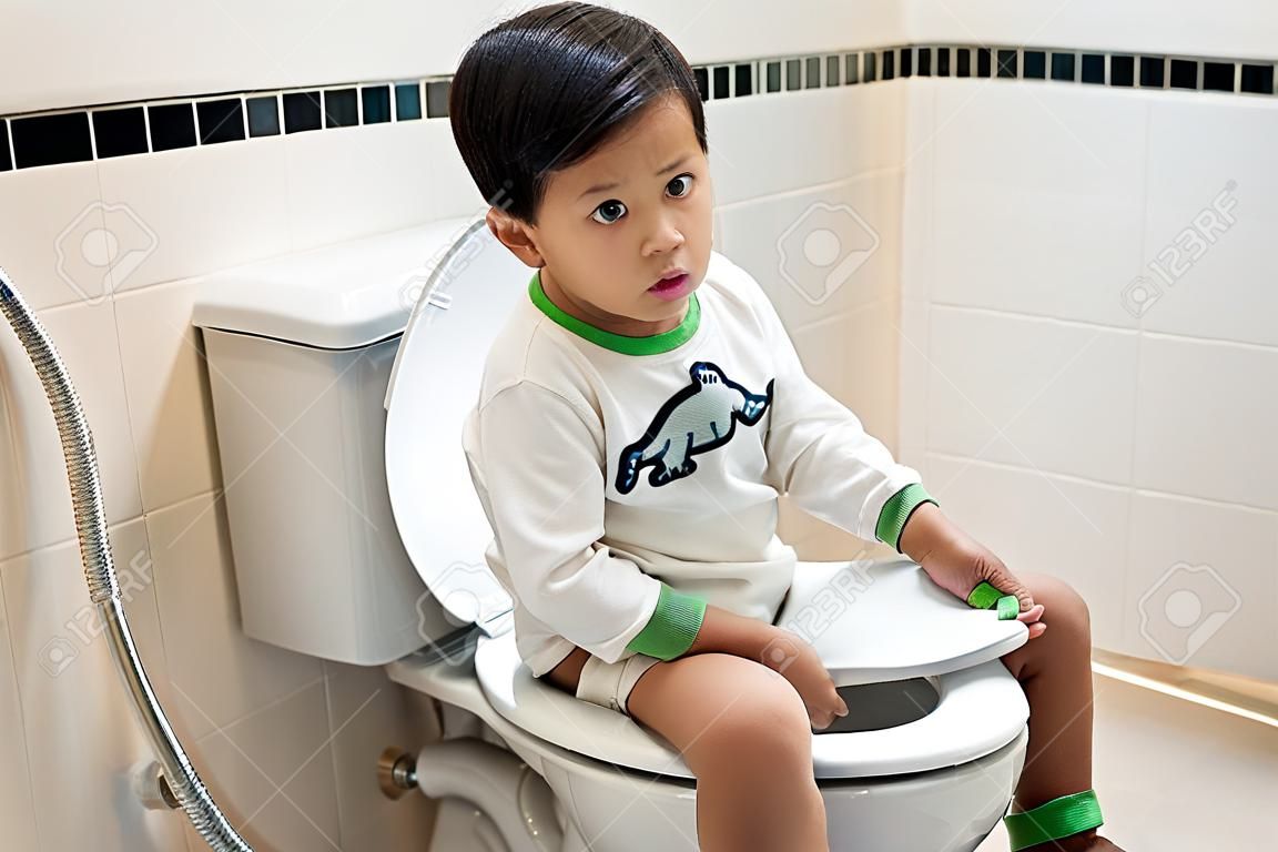Chłopiec siedzi na toalecie z zaparciami lub hemoroidami.