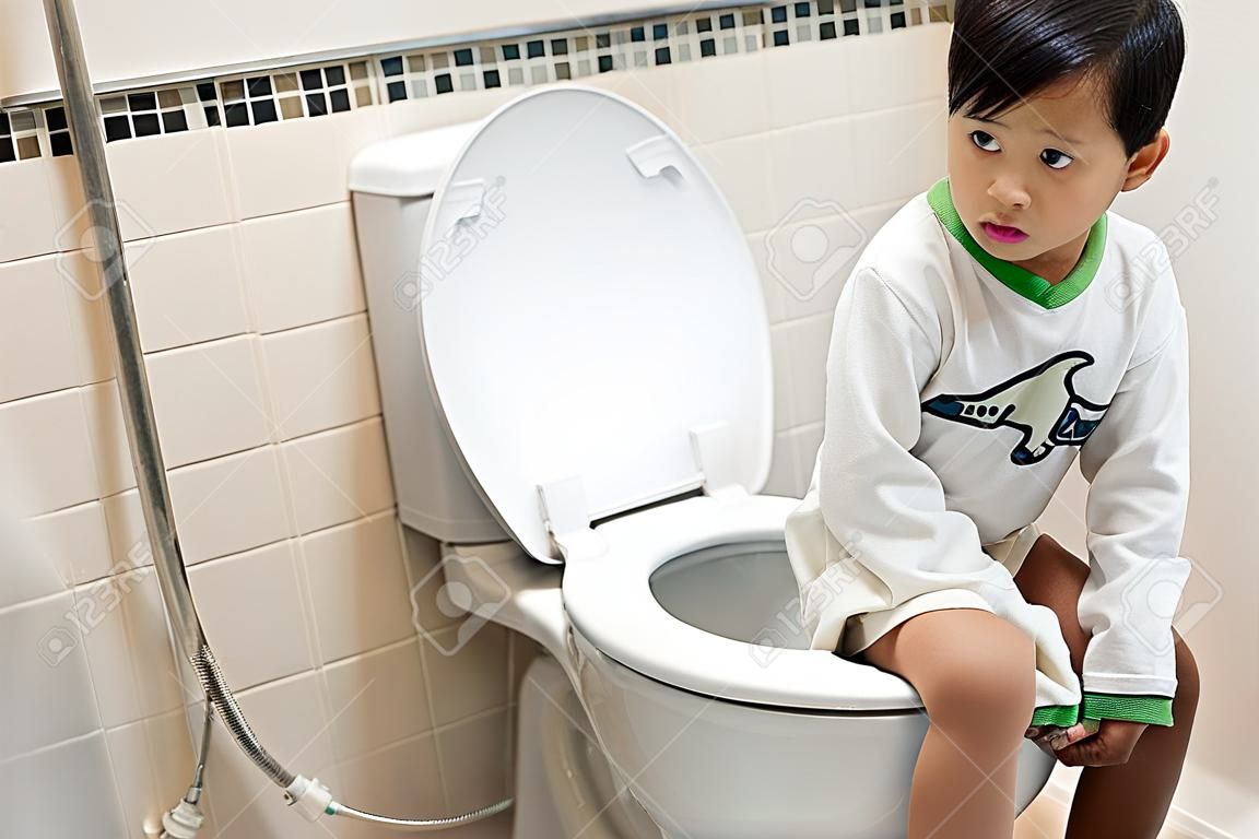 Chłopiec siedzi na toalecie z zaparciami lub hemoroidami.