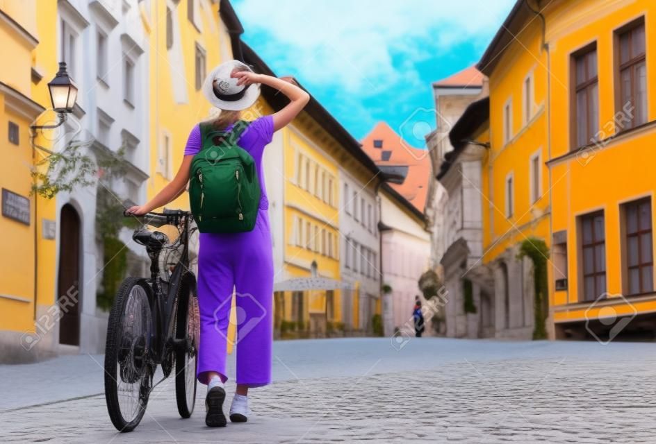 Viajar Eslovênia, Europa. Menina jovem com mochila e bicicleta urbana na rua velha no centro histórico de Liubliana. Mulher viajante explora pontos turísticos da cidade europeia. Morando local em Liubliana.