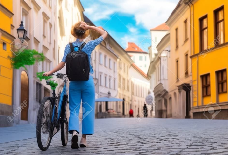 Viaja por Eslovenia, Europa. Chica joven con mochila y bicicleta urbana en la calle vieja en el centro histórico de Ljubljana. Mujer viajero explora lugares de interés de la ciudad europea. Vida local en Ljubljana.