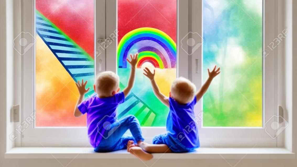 Małe dzieci na tle malarstwa tęczy na oknie. zdjęcie wypoczynku dzieci w domu. pozytywne wsparcie wizualne podczas kwarantanny pandemicznej koronawirusa covid-19 w domu. rodzinne tło
