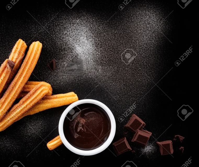 液体チョコレートとチュロス。チュロ - 黒の背景に砂糖パウダーと揚げ生地ペストリー。