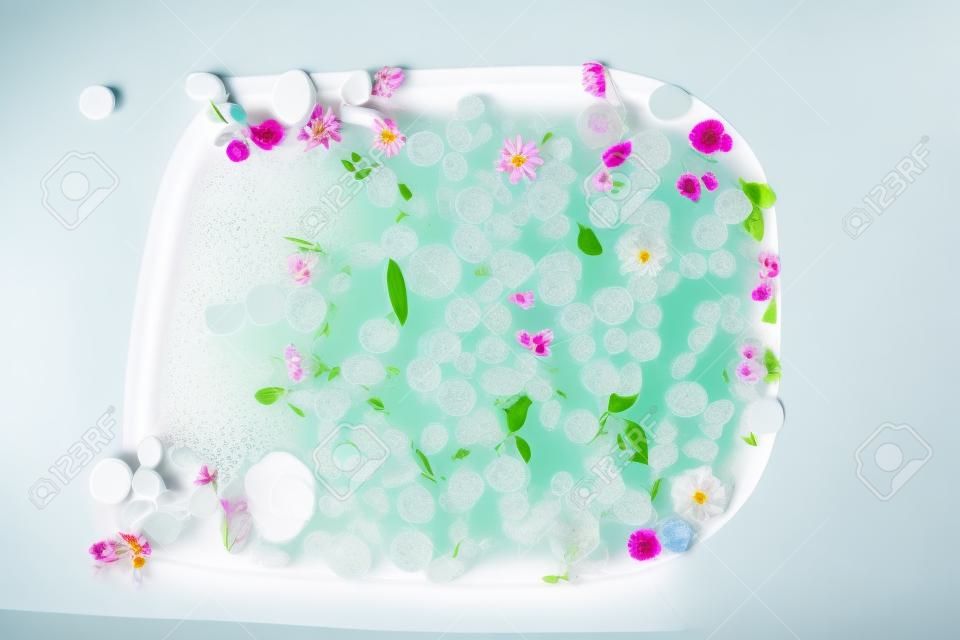 Vista superior do banho cheio de água da bolha, flores e pétalas, spa ou conceito do autocuidado