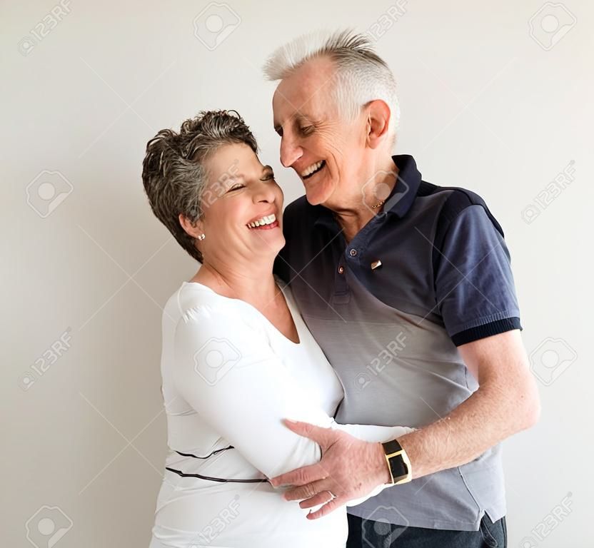 Vista de la longitud media de hombre mayor y una mujer con los brazos alrededor de la otra, riendo