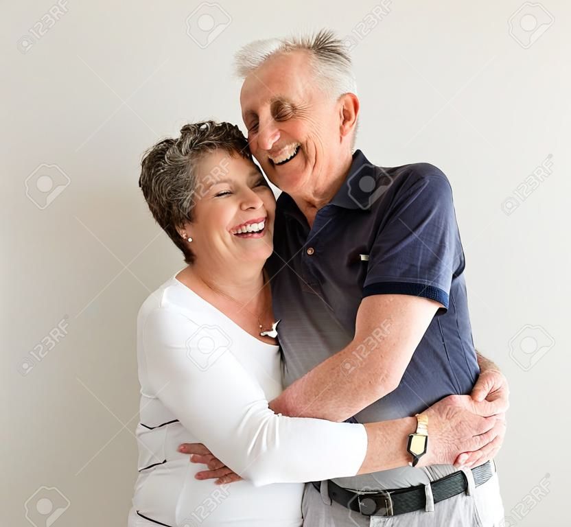 Vista de la longitud media de hombre mayor y una mujer con los brazos alrededor de la otra, riendo