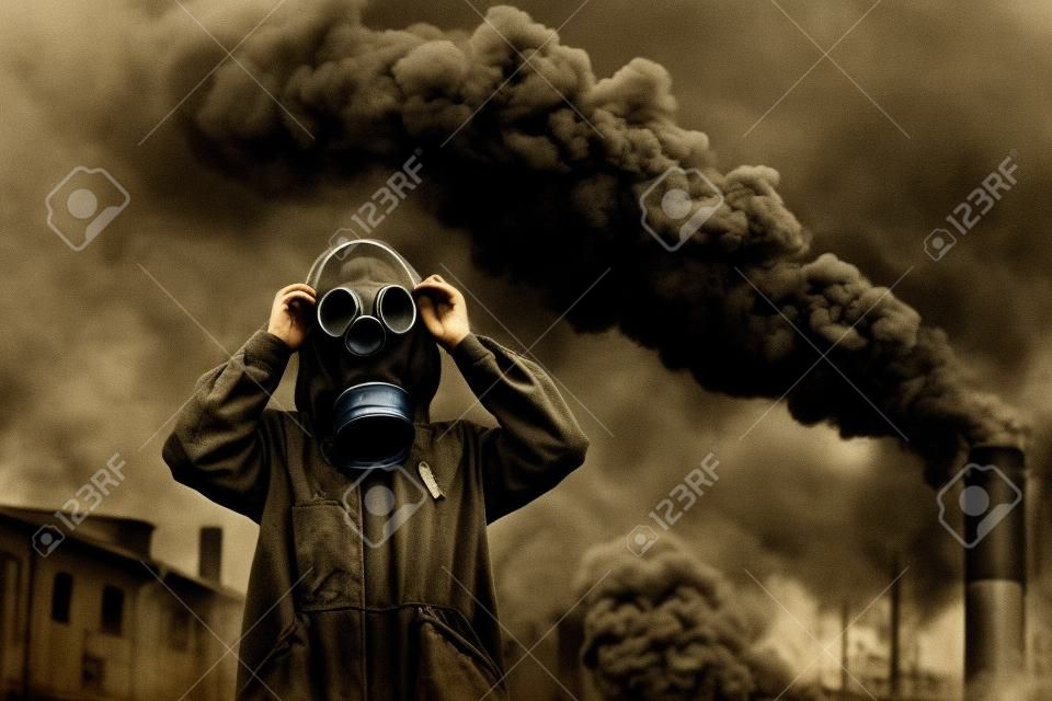 Het concept van luchtverontreiniging, ecologie. Een jong meisje in een gasmasker tegen de achtergrond van de rookfabriek schoorstenen. Getinte foto.