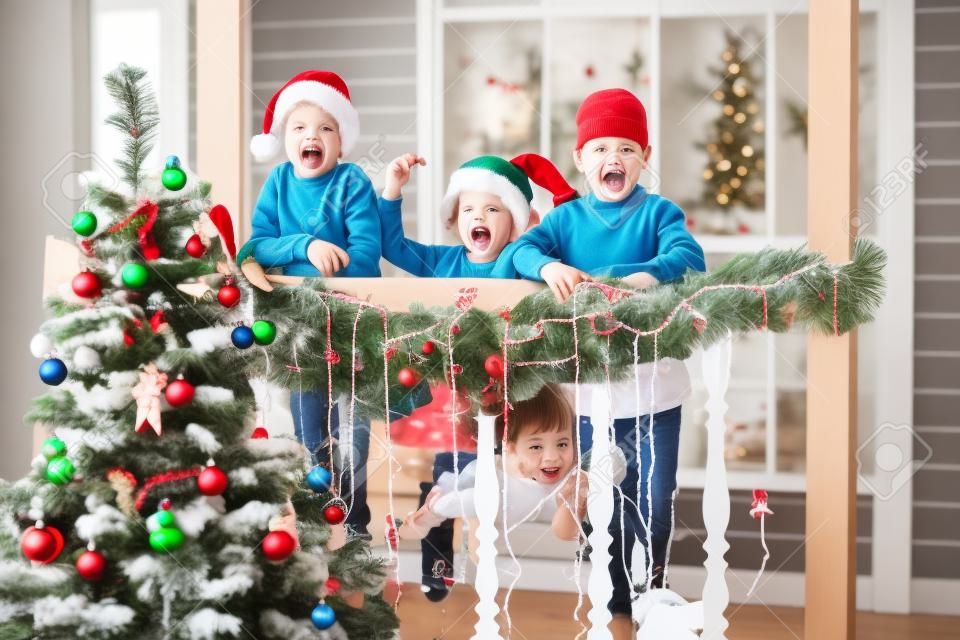 Kleine Kinder In Vorfreude auf Neujahr und Weihnachten. Drei kleine Kinder haben Spaß und spielen in der Nähe des Weihnachtsbaums im Innenraum mit Weihnachtsdekorationen