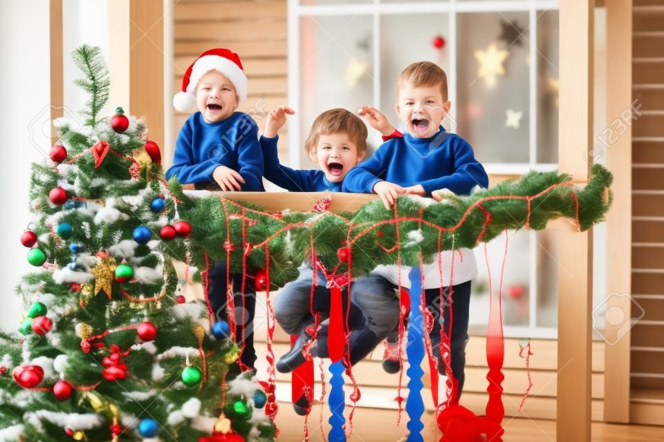 Bambini piccoli In previsione del nuovo anno e del Natale. Tre bambini piccoli si divertono e giocano vicino all'albero di Natale all'interno con decorazioni natalizie