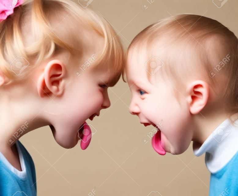 Two little girls unfriendly stick out tongues teasing each other