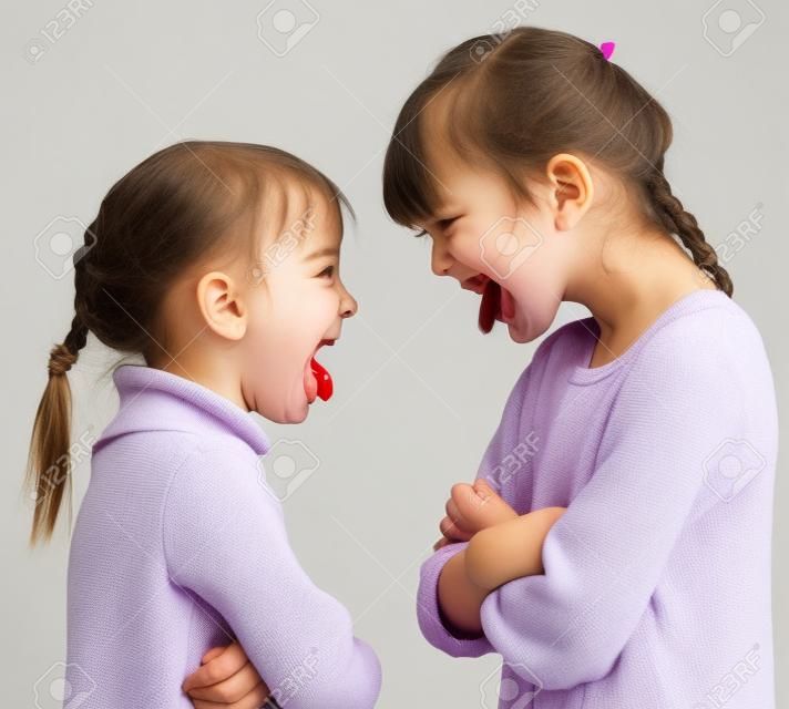 Two little girls stick out tongues teasing each other