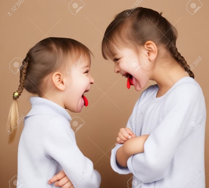 Two little girls stick out tongues teasing each other
