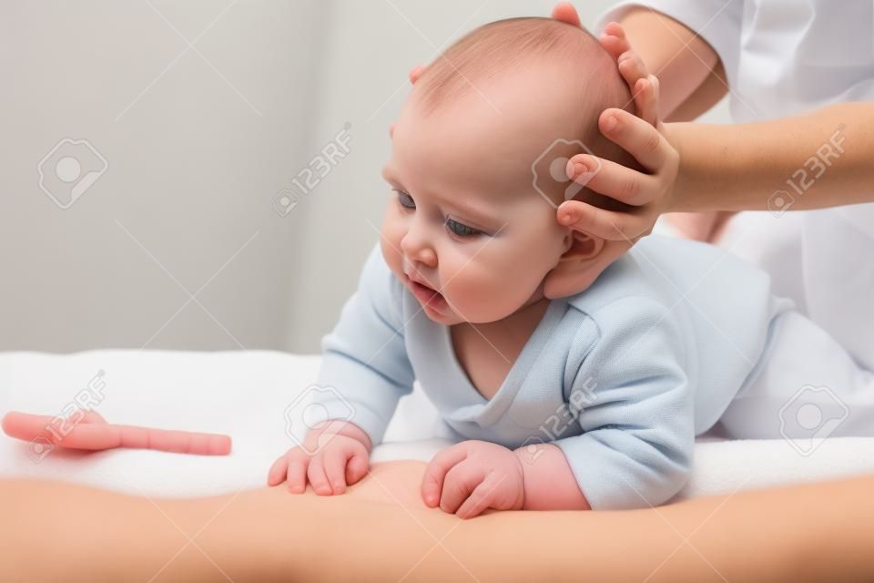 Six month baby girl receiving osteopathic or chiropractic treatment in pediatric clinic. Manual therapist manipulates chils's head and neck