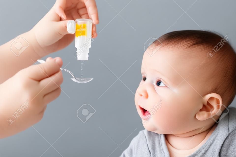 Mother feeding baby boy with vitamin or liquid medicine using spoon