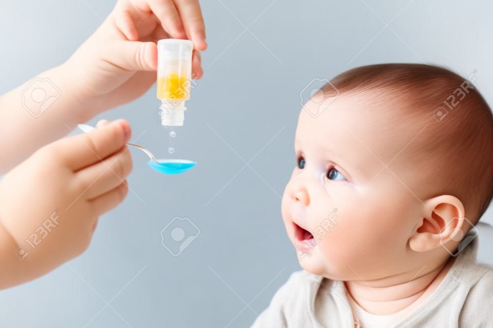 Matka karmiąca chłopca witaminą lub płynnym lekiem za pomocą łyżki