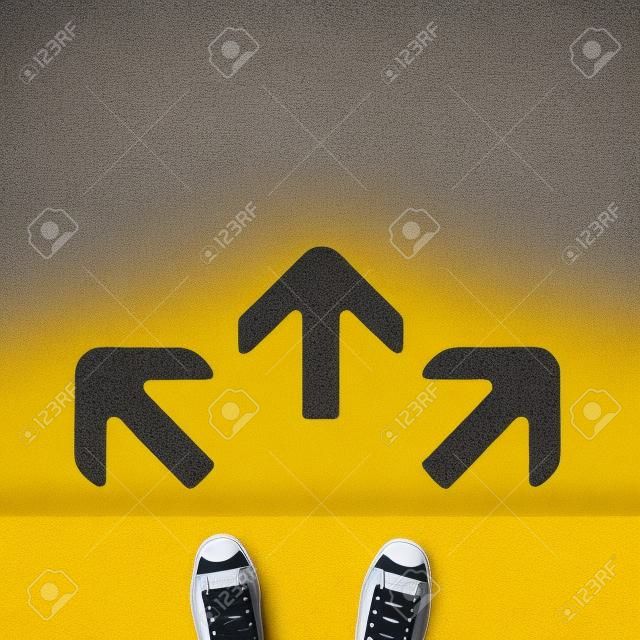 Paio di scarpe in piedi su una strada con tre freccia grigia su sfondo giallo