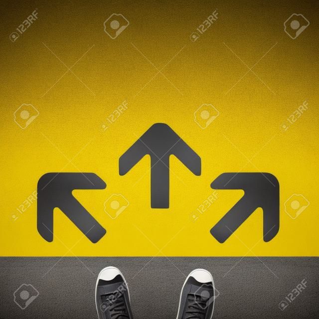 Paio di scarpe in piedi su una strada con tre freccia grigia su sfondo giallo
