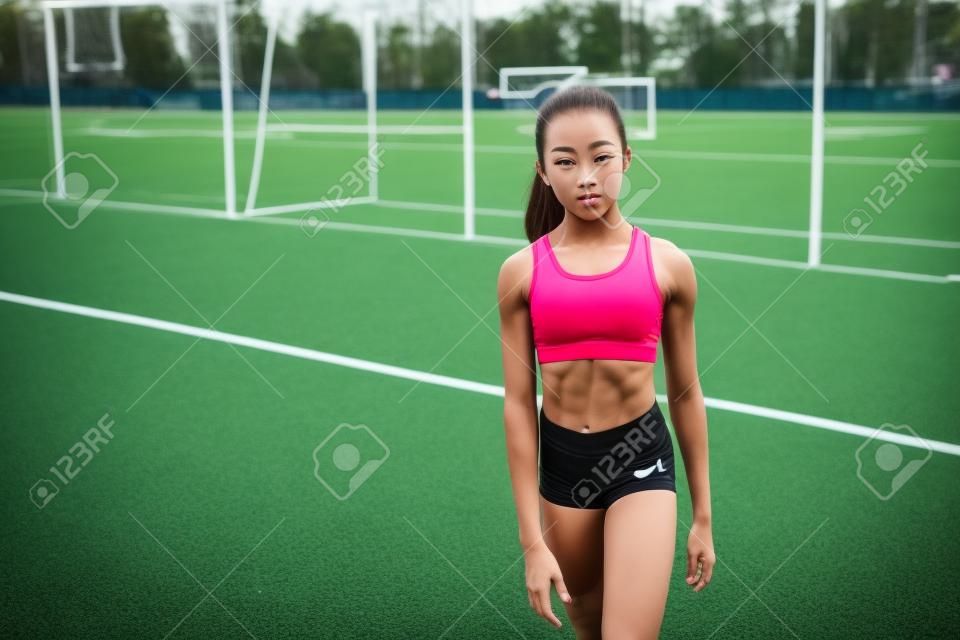 Jong mooi meisje van een slanke body building, gekleed in een sport uniform, brengt tijd door op een sportveld. Lifestyle