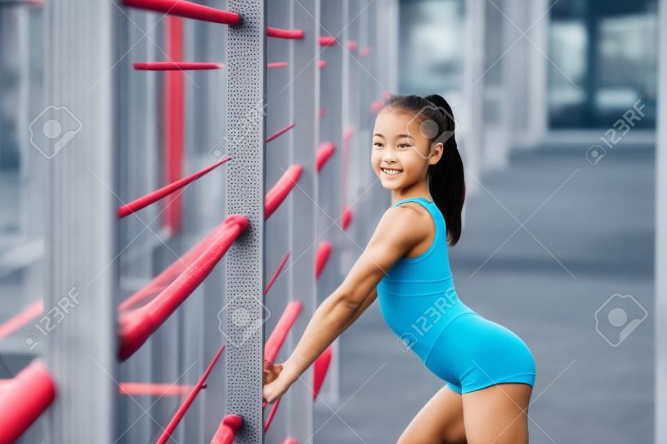 Een jong, sympathiek meisje van slank body building, gekleed in een vorm van sport, voert gymnastiek oefeningen in de open lucht. Lifestyle
