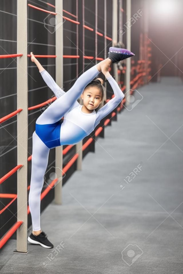 Een jong, sympathiek meisje van slank body building, gekleed in een vorm van sport, voert gymnastiek oefeningen in de open lucht