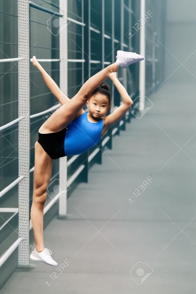Uma jovem, simpática menina de esbelto edifício do corpo, vestida em uma forma de esporte, realiza exercícios de ginástica ao ar livre