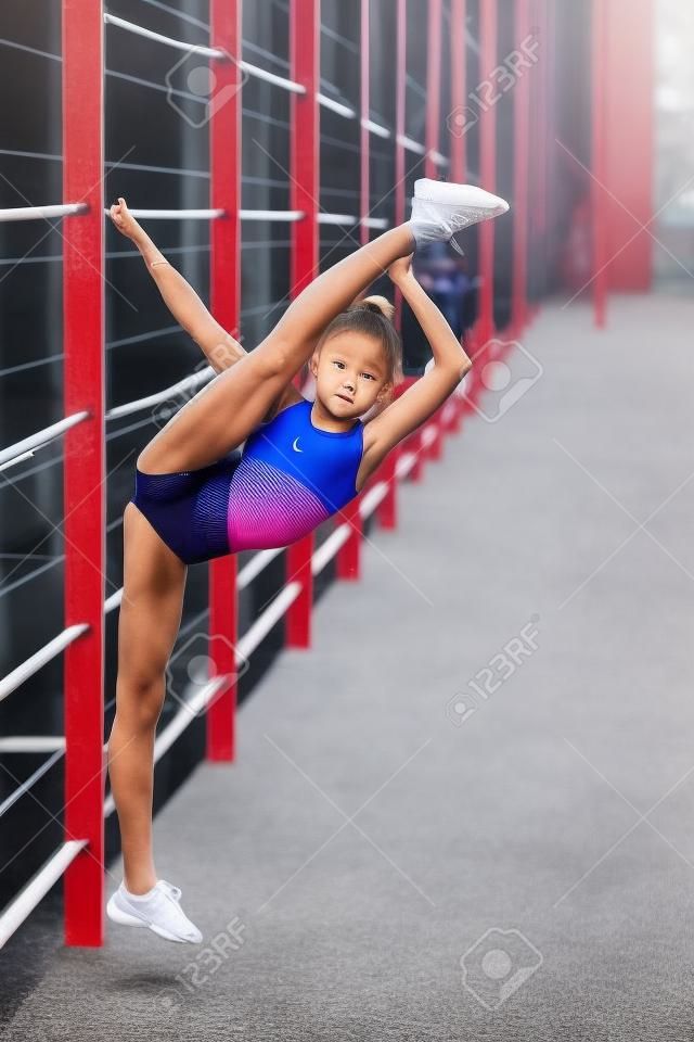 Ein junges, sympathisches Mädchen mit schlankem Bodybuilding, das in einer Sportart gekleidet ist, führt gymnastische Übungen im Freien durch
